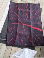 Floor mat laid out flat showing black surface with red crack-like pattern.