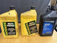 Photo of three bottles of automatic transmission fluid, two SureGuard brand in yellow bottles and one Certified brand in a black bottle, all labeled for use in automatic transmissions.