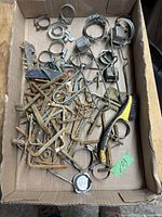 Box containing used metal hose clamps, strikers, Allen keys, a cleaning brush, and various metal fasteners with rust and wear.