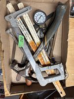 Photo of box containing various used hand tools including a staple gun, pressure gauge, hand saw handles, and hammers.
