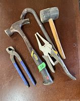 Photo shows five hand tools including a claw hammer, rubber mallet, two pliers, and an adjustable wrench.
