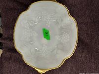Top view of white milk glass dish with embossed grape and leaf relief and gold tone scalloped edges.