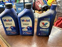 Three blue 1-quart bottles of automatic transmission fluid on a table: two Mobil Dexron-VI and one Valvoline Dexron-V full synthetic.