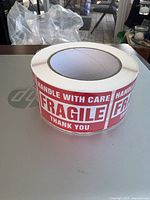 Large roll of adhesive fragile stickers with clear red and white text reading HANDLE WITH CARE FRAGILE THANK YOU