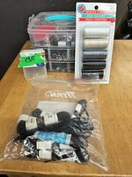 Overall view of the sewing kit contents including a plastic compartment box with sewing notions, loose spools of black colored thread in a plastic bag, and a 6-spool unopened pack of Craft Brand sewing thread in neutral colors