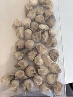 Close-up photo showing approximately 40 small skull-shaped beads with carved details and natural stone texture, arranged closely together on a white background.