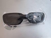 Photo of black rectangular sunglasses sealed in the original clear plastic wrapping.