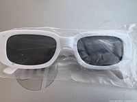 Photo of white frame sunglasses with dark lenses still in clear plastic packaging