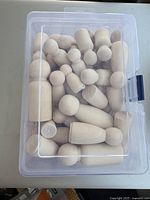 Clear plastic container filled with multiple plain wooden peg dolls in different sizes, shown from top down.