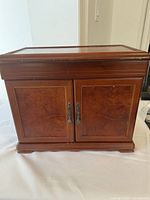 Closed view of the antique wood jewelry box showing front panel with two cabinet doors and metal handles.