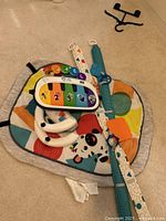 Overall view of the multi-color Baby Einstein play mat, interactive piano, and tethered plush toys arranged on a carpeted floor.