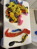 Multiple deflated inflatable party favor toys on a white surface including guitars, microphones, and saxophones in red, yellow, blue, and pink colors.