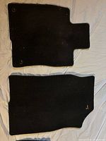 Black carpet front and rear floor mats on white background, showing general condition and securing snap buttons.