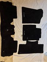 Five black cloth car mats laid out on a light surface, showing sizes and logos for Infiniti QX80, including larger front mats and smaller rear/middle mats.