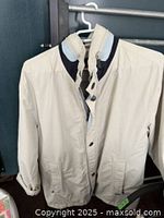 Off-white men's rain jacket hanging on a hanger showing front view with snap buttons and collar detail.