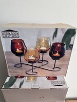 Box showing Simply Home Solutions branding and image of candle holders with 4 colored glass cups set on black metal twisted base