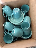 Top-down view of the turquoise ceramic mugs and plates packed in a box showing glossy finish and ring pattern detail.