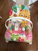 Front view of the rocker chair showing the pink jungle themed cushion with animal prints and attached toy bar with tiger and butterfly toys.