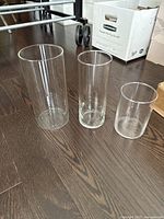 Set of three glass cylinder vases in large, medium, and small sizes together on dark wooden floor.