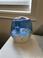 Front view of the Homasy blue and white electric humidifier on a table near window.