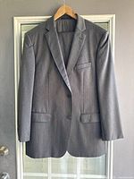 Grey two-button blazer hanging on a wooden hanger, showing the full frontal view with flap pockets and chest pocket.