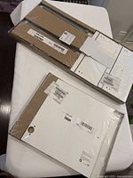 Two sealed IKEA Kallax inserts on a white cloth surface, one appears to be the cupboard insert and the other the drawer insert, both with original packaging labels visible.