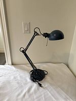 Blue IKEA FRSA desk lamp shown side view, adjustable arm extended, lamp head angled down.