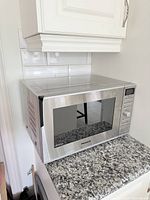 Panasonic stainless steel microwave on granite countertop under white cabinetry