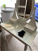 White Hemnes vanity table with glass top, oval mirror, two side drawers, and black gloves on the surface.