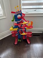 Side view of the Little Tikes Take Turns car tower showing the red and yellow spiral track, blue support frame, and flags on top.