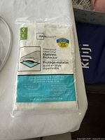 Front packaging view of Mainstays waterproof fitted vinyl mattress protector showing brand, size (queen), and features such as machine washable and waterproof.