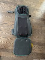 Top down view of black travel massage chair laid flat on wood floor with remote control attached.