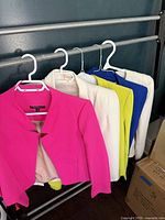 Five women's blazers hanging on rack in various bright colors including hot pink, cream, yellow, blue, and white.