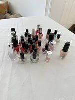 Overhead photo showing a cluster of approximately 30 nail polish bottles of various brands and colors on white surface