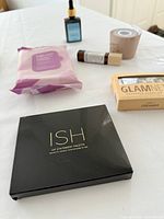 Photo of the ISH Lip Statement Palette along with other beauty items on a white surface, including cleansing wipes, hair oil in a blue bottle, a beige roll-on bottle, Glamnetic nails box, and a beige scalp massager.