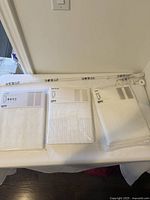 Three sealed packages of white IKEA curtains LILLEGERD and one white curtain rod laid out on a surface.
