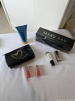 Photo showing black Mary Kay makeup pouch, tube of hand cream, Mary Kay lipstick holder box, and two lipstick boxes arranged on white surface