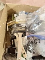 Box containing paint brushes with wooden handles and other home hardware items.