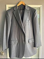 Front view of the grey pinstripe blazer on a hanger, showing lapel, pockets, button closure, in natural light.