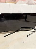 Samsung black flat-screen TV on dual leg stand with white styrofoam packaging on edges