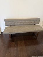 Front view of the grey upholstered dining bench showing the tufted backrest and seat cushion, sitting on wooden legs.
