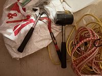Hand tools including a claw hammer and rubber mallet on top of a white fabric bag, along with coiled extension cords.