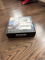 Closed black and blue Alvoxcon USB condenser microphone box on wooden floor, showing front of packaging with product name and branding.