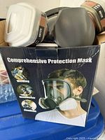 Respirator mask kit in original box labeled 'Comprehensive Protection Mask' showing the mask with attached 6001CN filters and illustration of usage scenarios.