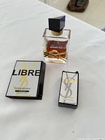 Top view of the full size perfume bottle with gold YSL logo, a sampler vial in branded box, and their packaging on a white surface.