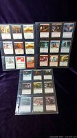 Three clear plastic sleeves containing 27 Magic: The Gathering cards laid out showing card fronts with various artworks and text from different sets.