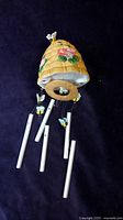 Front view of ceramic beehive top with floral and bee decorations, metal chime rods hanging below