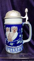 Front view of Goebel Bavarian Forest stoneware stein with two owls and handle, pewter lid closed.