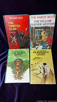 Four Hardy Boys books with colorful dust jackets showing front cover artwork and titles: The Twisted Claw, The Yellow Feather Mystery, The Masked Monkey, The Mysterious Caravan.