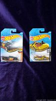 Two Hot Wheels toy cars side by side sealed in original packaging, one gold and one black.